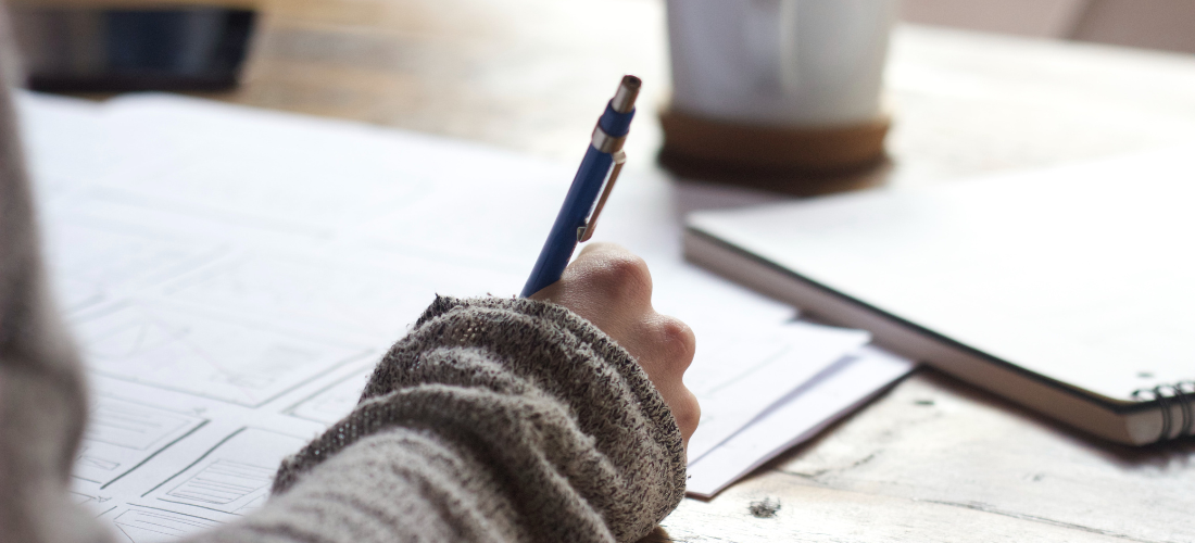 Hand holding a pen and writing in a notebook